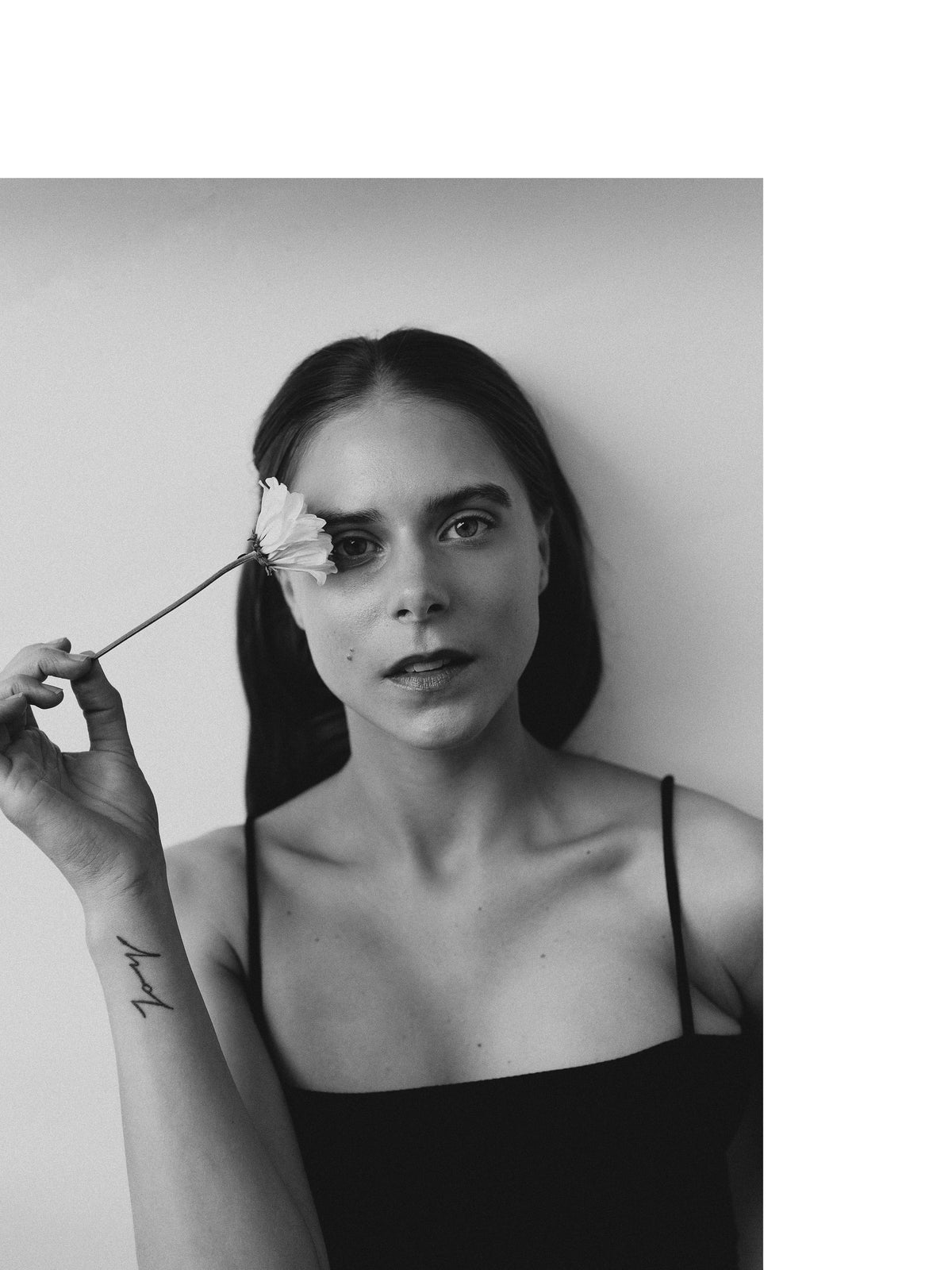Black-and-white portrait of a woman looking toward the camera while holding a flower beside one eye.