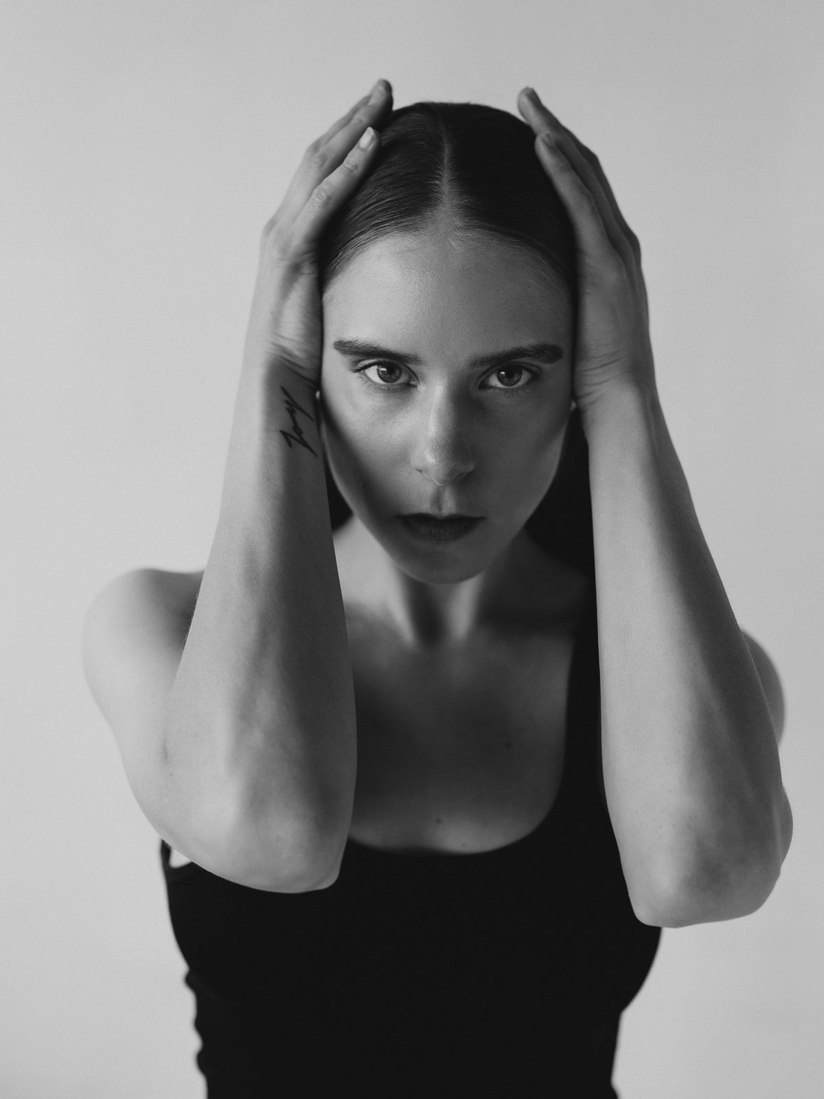 Black-and-white portrait of a woman looking directly toward the camera, both hands framing her head.