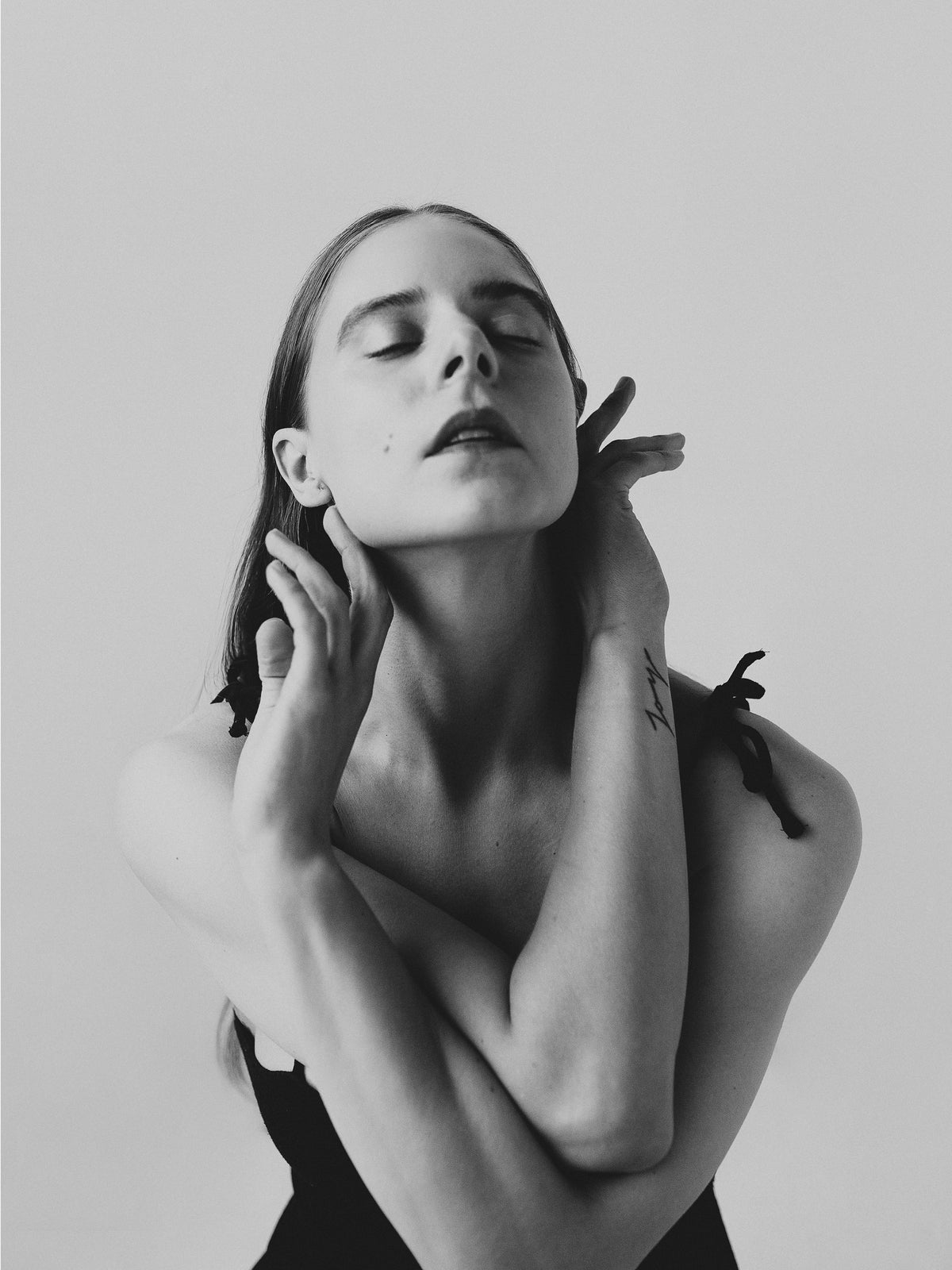 Black-and-white portrait of a woman with closed eyes and crossed arms, her hands resting beside her neck.