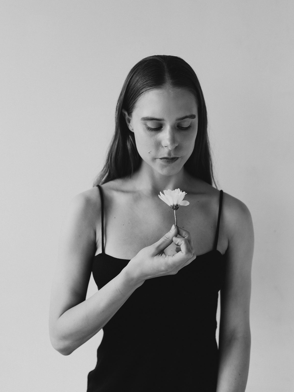Black-and-white portrait of a woman looking down at a flower held near her chest.