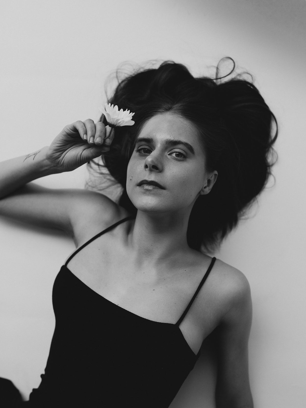 Black-and-white portrait of a reclining woman holding a flower beside her head, her hair spread out behind her.