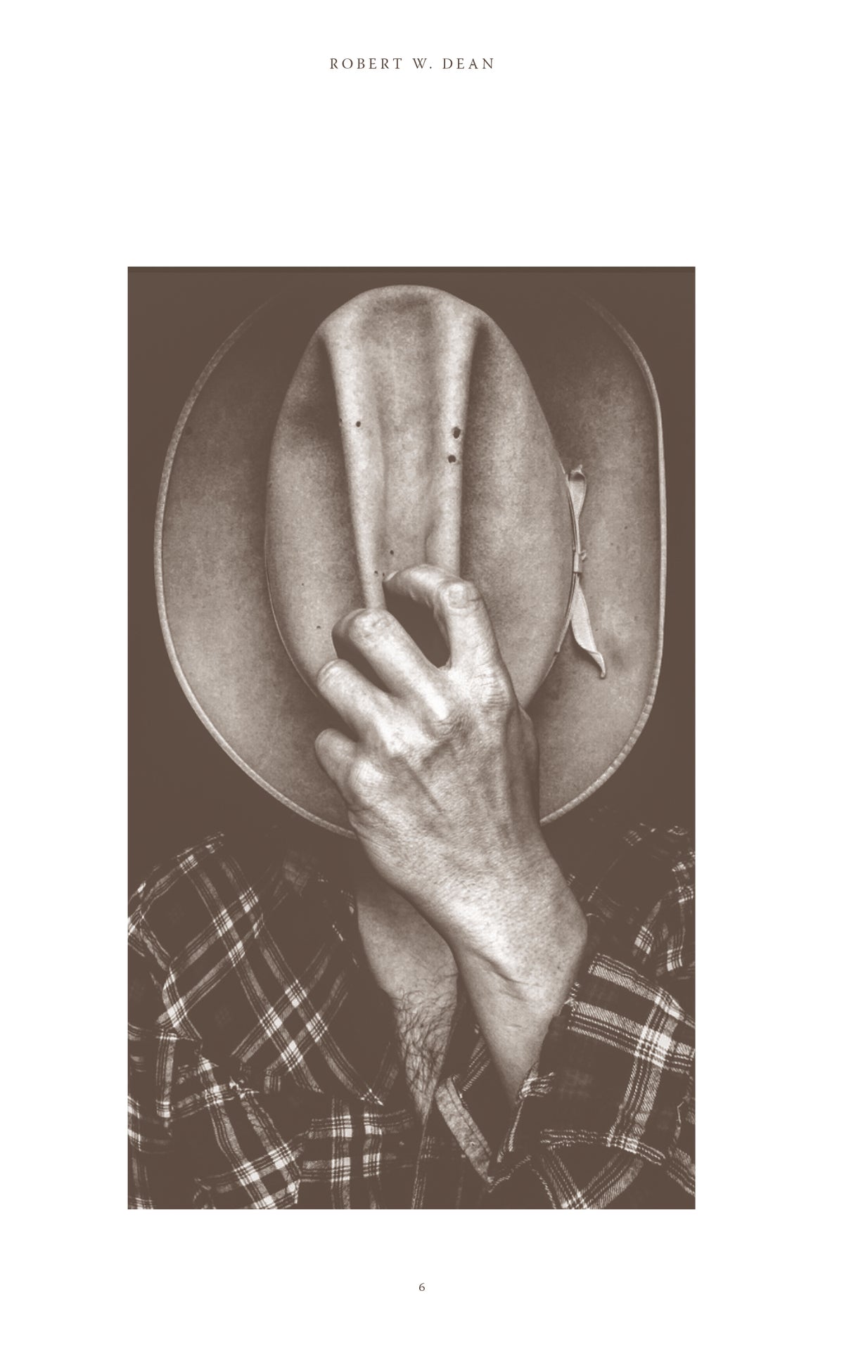 Sepia photograph of a person in a plaid shirt holding a cowboy hat over their face.