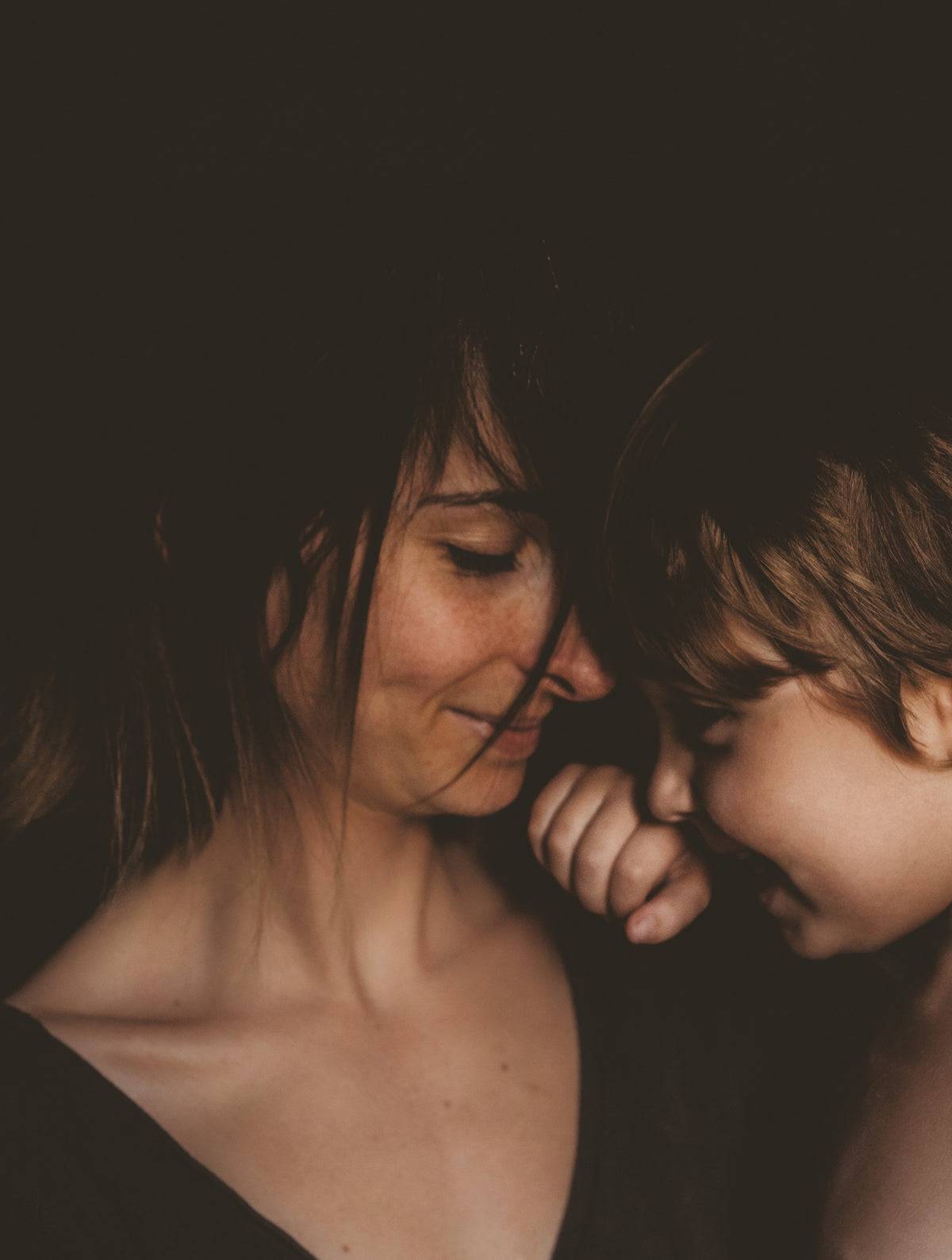 Close-up portrait of a woman and a child leaning their heads together, with their eyes lowered.